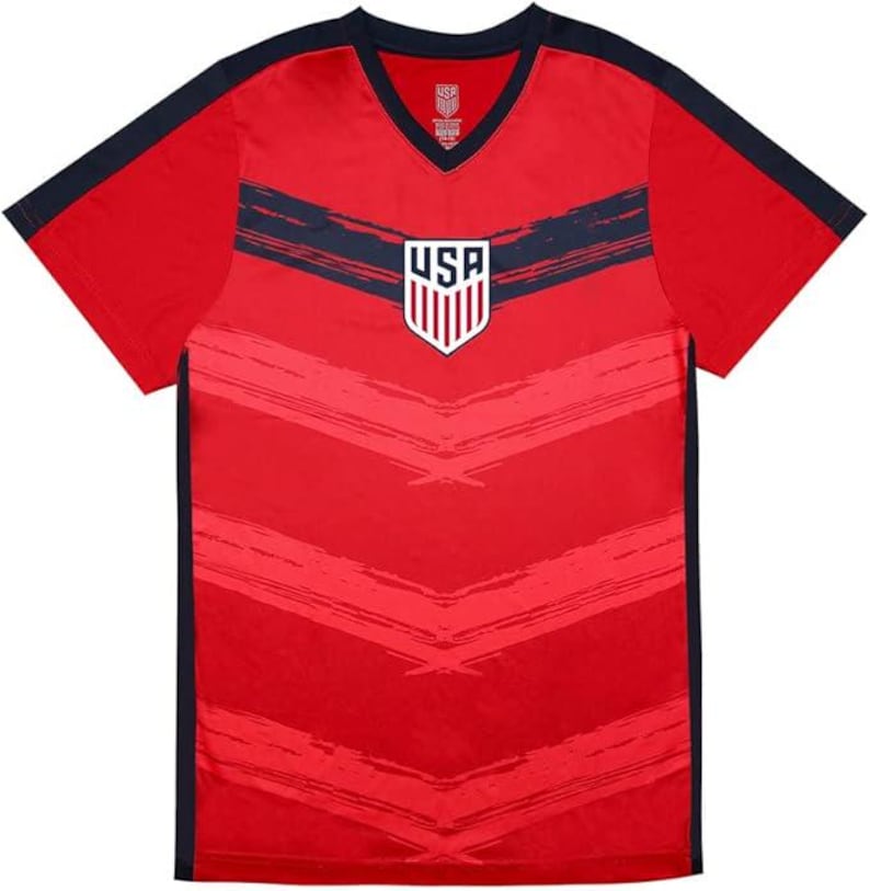 May include: Red V-neck t-shirt with navy blue accents on the sleeves and shoulders. The shirt features a navy blue horizontal stripe across the chest and a USA emblem. The shirt has a textured design.