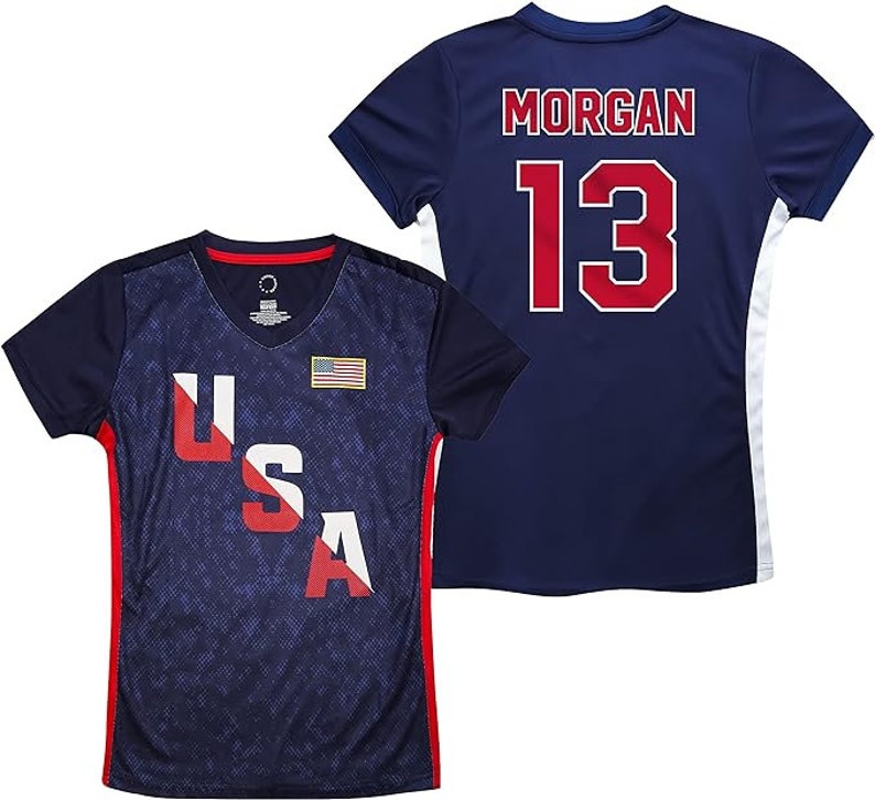 Pu&ograve; includere: Due maglie da calcio blu navy. Una maglia ha il testo "USA" in rosso, bianco e blu con una piccola bandiera americana sul petto. L'altra maglia ha il testo "MORGAN" e il numero "13" in rosso.
