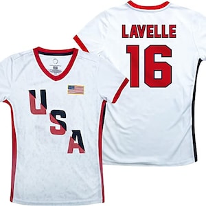 May include: White jersey with red and blue trim. The jersey has the word "USA" in red, white, and blue letters on the front and a small American flag. The back of the jersey has the name "Lavelle" and the number "16" in red.
