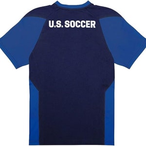 May include: A navy blue short-sleeved t-shirt with royal blue sleeves and side panels. The back of the shirt has the text "U.S. SOCCER" printed in white.