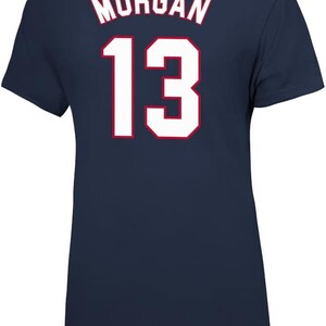 May include: Navy blue t-shirt with white lettering. The text on the back of the shirt reads "MORGAN 13".