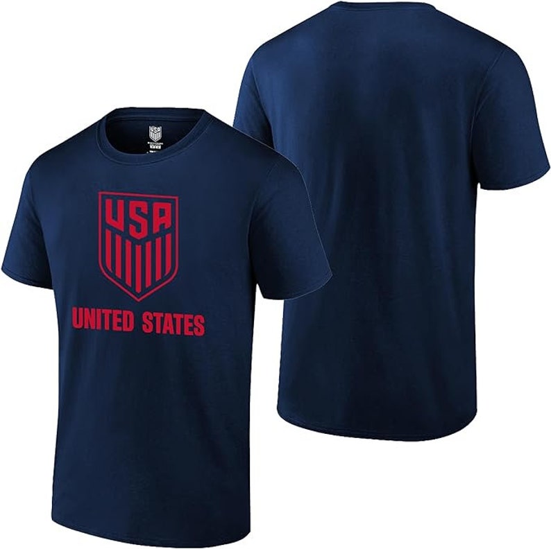 Puede incluir: Camiseta azul marino con un escudo rojo de EE. UU. y las palabras "UNITED STATES" impresas en la parte delantera.