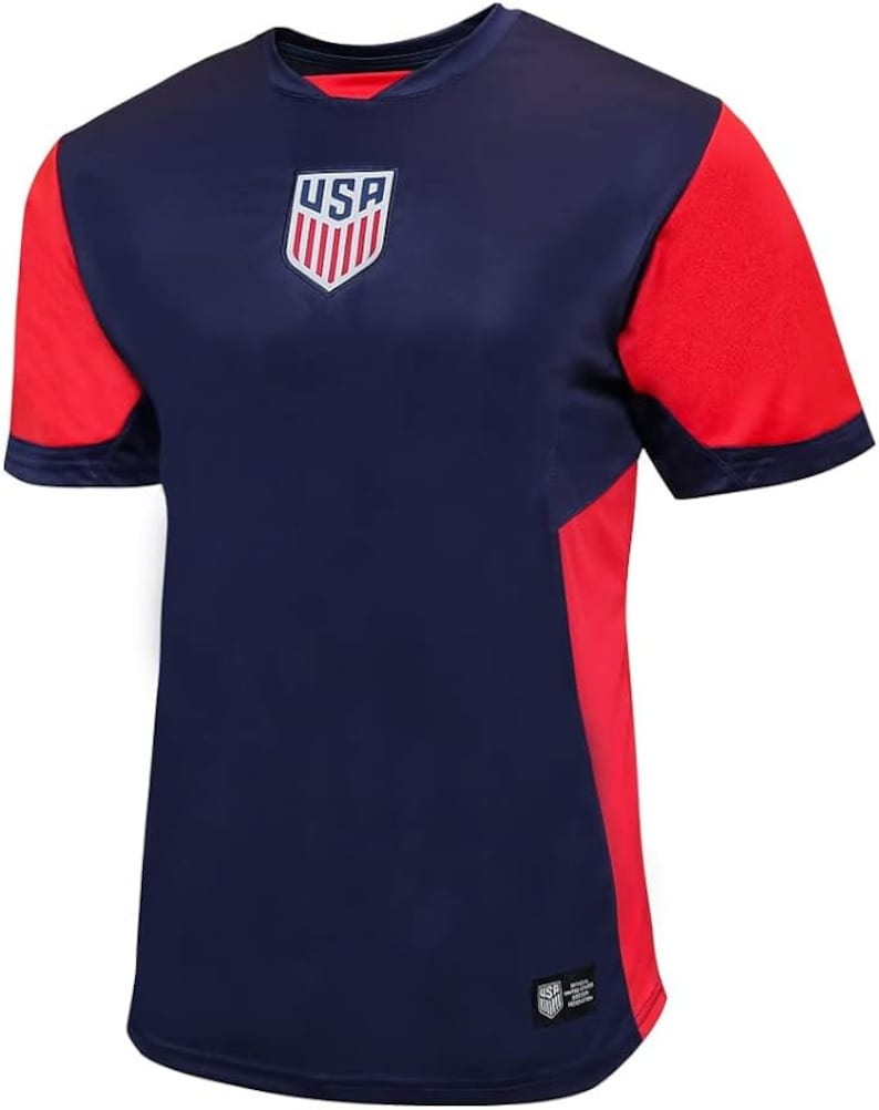 May include: A navy blue soccer jersey with red accents. The jersey has the word "USA" and a shield with red and white stripes on the front.