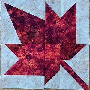 May include: A patchwork maple leaf block, featuring a red and orange leaf design set against a light beige background. The leaf pattern is constructed from multiple fabric pieces, creating a unique patchwork design. Ideal for quilting projects, the block measures approximately 20 cm x 20 cm.