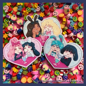 May include: A collection of stickers featuring anime-style characters with bunny ears, drinking beverages. The stickers are heart-shaped and surrounded by colorful fruit-shaped erasers. The characters have various hair colors and expressions.