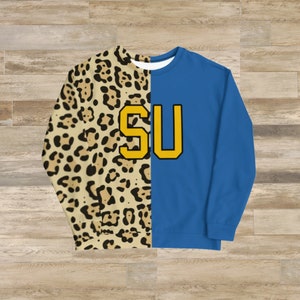 May include: A blue and leopard print sweatshirt with the letters "SU" in yellow on the front.