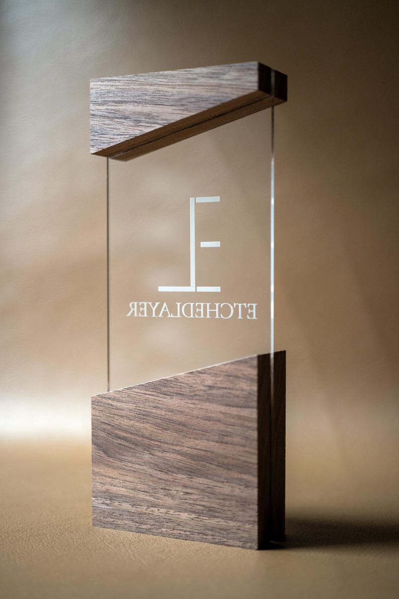 May include: A clear glass sign with the text "ELCHEDHOTEL" in white, framed by dark wood at the top and bottom. The sign has a modern, minimalist design, suitable for a hotel or business.