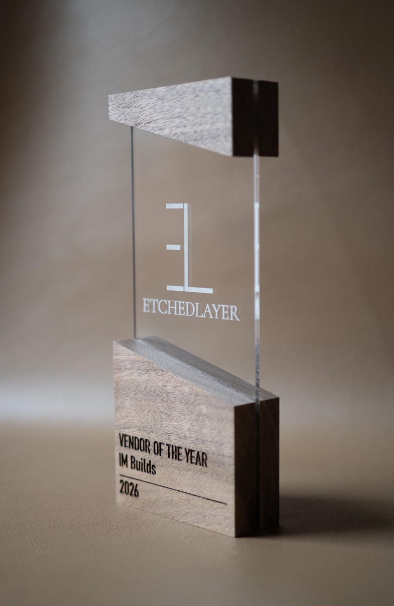 May include: A clear acrylic award with wooden accents. The award features the text "ETCHEDLAYER" and "VENDOR OF THE YEAR IM Builds 2026". The design is modern and minimalist, with a focus on clean lines and contrasting materials.