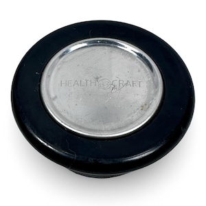 May include: A black and silver Health Craft lid. The lid has a black outer ring and a silver center with the text "HEALTH CRAFT" printed on it. The lid is circular and appears to be made of metal and plastic.