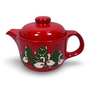 May include: A red ceramic teapot with a lid and handle. The teapot features a Christmas tree and goose design in green and white. The teapot is a festive item for serving tea.