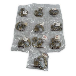 May include: Ten individual brass-toned metal drawer pulls, each enclosed in a clear plastic bag. Each pull features a curved, ornate design with a mounting screw visible inside the packaging. The brand name Belwith is printed on each bag.