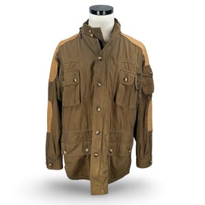 May include: Olive green jacket with multiple front pockets, tan shoulder patches, and button closures. The jacket has a high collar and a zipper. A classic, durable outerwear piece.