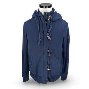 May include: A navy blue hooded sweatshirt with a zipper and wooden toggle closures. The jacket has a drawstring hood, two front pockets, and a small patch on the upper arm. The sweatshirt is displayed on a mannequin.