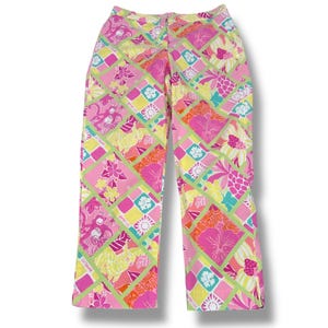 May include: Pink, yellow, and green patterned pants with a floral and geometric design. The pants feature a vibrant mix of colors and patterns, including flowers, monkeys, and geometric shapes. The pants have a straight leg cut and a zipper closure.