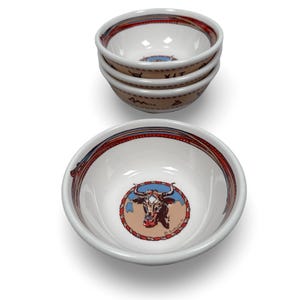 May include: Set of four white ceramic bowls with a Western theme. Each bowl features a red, blue, and tan rim design. The interior of each bowl has a bull graphic in a circular frame. The bowls are stacked.