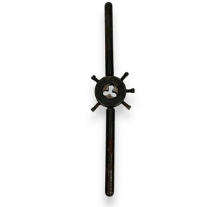 May include: A vintage tap wrench tool, featuring a dark, aged metal finish. The tool has a central circular component with a three-lobed opening, surrounded by six small, evenly spaced projections. Two long, parallel handles extend from the central component.