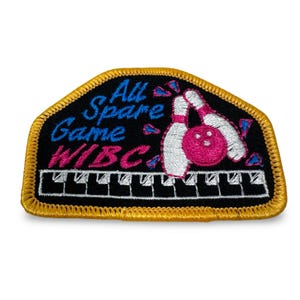 May include: Embroidered patch with a black background and gold trim. The patch features the text "All Spare Game WIBC" in blue and pink, along with bowling pins and a ball. A piano keyboard design is at the bottom.