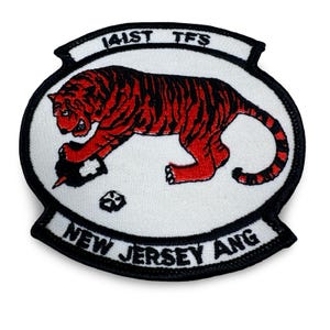 May include: Embroidered patch featuring a red and black tiger clutching a black object. The patch has a white background with the text "141ST TFS" and "NEW JERSEY ANG" in black.