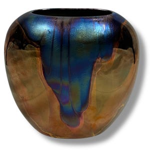 May include: A decorative iridescent glass vase with a wide, rounded shape. The vase features a dark blue and gold color scheme with a glossy finish. The vase has a dark interior and a smooth exterior.