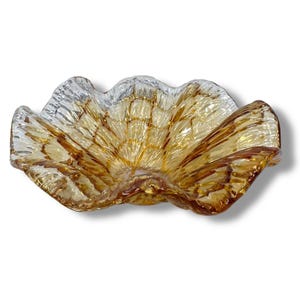 May include: A decorative glass bowl with a ruffled, shell-like design. The bowl features a blend of amber and clear glass, with a textured surface. The bowl's shape is reminiscent of a flower or seashell.