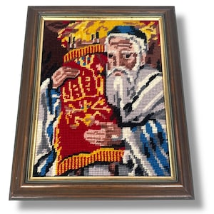 May include: A framed needlepoint embroidery depicting a man with a long white beard holding a red and gold Torah scroll. The man is wearing a traditional Jewish prayer shawl with blue and white stripes.