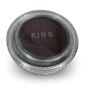 May include: A clear glass jar with a dark brown substance inside. The word "KING" is embossed in the center of the jar. The jar has a ridged, textured edge.