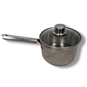 May include: A small, stainless steel saucepan with a long handle and a clear glass lid. The lid has a small, round metal handle. The saucepan is designed for cooking and has a slightly worn appearance.