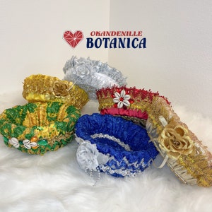 Peut inclure: Six paniers décoratifs à bords festonnés, chacun avec une couleur et un design différents. Les paniers sont en tissu et ont des garnitures dorées. Les paniers sont disposés sur une surface blanche et moelleuse. Le texte "OKANDENILLE BOTANICA" est visible dans le coin supérieur droit de l'image.