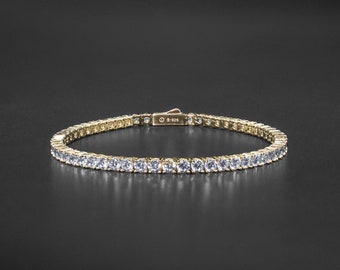 May include: A gold tennis bracelet with a row of clear round cubic zirconia stones.