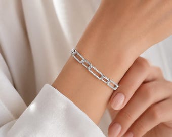 May include: A silver-toned chain link bracelet featuring rectangular links. Each link is encrusted with small, clear, sparkling stones along the outer edges, creating a continuous shimmering effect around the wrist in a classic link design.