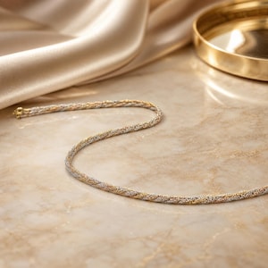May include: A multi-toned chain necklace featuring a braided design with alternating strands of yellow gold, rose gold, and silver-colored metal. The chain has a smooth, textured appearance and includes a small circular clasp at one end.