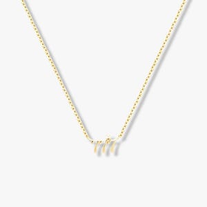 May include: A gold-coloured necklace with a pendant displaying the number "777" in a decorative style. The necklace has a fine chain and is set against a plain backdrop. The pendant includes a small, sparkling detail.