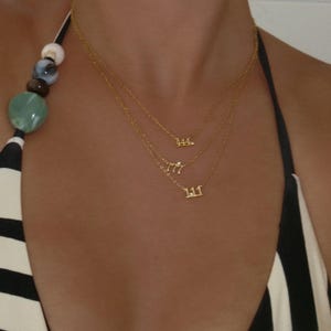 May include: Three fine gold necklaces, each with a number pendant: 111, 777, and 444. The necklaces are layered, offering a minimalist style. The background features a black and white striped pattern.