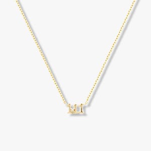 May include: A gold-coloured necklace with a pendant displaying the number "111". The pendant is small and hangs from a fine chain. The necklace is shown against a plain background.