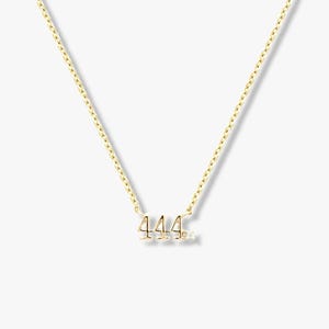 May include: A gold-tone necklace with the number "444" as a pendant, accompanied by a small diamond. The chain is fine and elegant. The necklace is presented on a neutral background. The necklace is suitable for everyday wear.