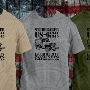 May include: Three t-shirts with a vintage military truck design. The shirts are in beige, gray, and green. The design features a Studebaker US-6 truck with the text "Studebaker US-6 1941-1945 G630105.917 6X6 UNITS PRODUCED".