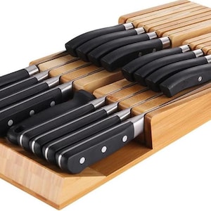 May include: A bamboo knife block organizer containing a set of kitchen knives with black handles and silver rivets. The wooden tray features multiple horizontal slots designed to hold the knives securely in a flat, organized arrangement.