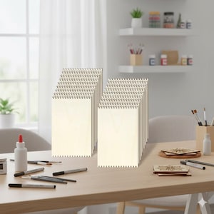 May include: Stacks of unfinished wooden panels with a spiral binding at the top. The panels are rectangular with a light wood grain finish. The image is taken on a light-colored wooden table with art supplies.