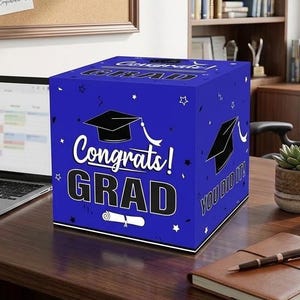 May include: A blue cubic graduation card box featuring white text that reads Congrats! GRAD and YOU DID IT!, decorated with black graduation cap icons, white diploma illustrations, and small star and confetti patterns on all visible sides.