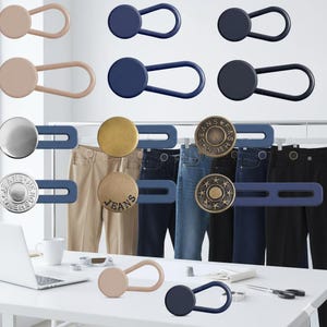May include: Assorted jean button extenders in various colors and styles. The extenders include beige, navy, and black options, with button designs in silver, gold, and bronze. Some extenders are attached to jeans.