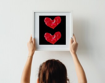May include: A white frame with a black background and two red hearts painted on it. The hearts are slightly overlapping and are in a vertical orientation.