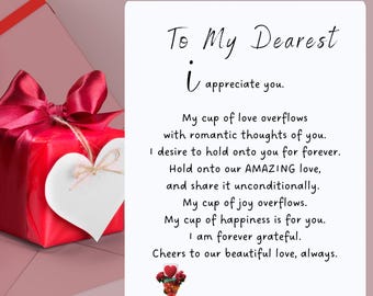 May include: A red gift box with a white heart on top, surrounded by a pink background. The text "Gift of Love" is at the top of the image, and the text "To My Dearest" is below it. The text "I appreciate you." is below that. The text "My cup of love overflows with romantic thoughts of you. I desire to hold onto you for forever. Hold onto our AMAZING love, and share it unconditionally. My cup of joy overflows. My cup of happiness is for you. I am forever grateful. Cheers to our beautiful love, always. Happy Valentine, my love." is below that.