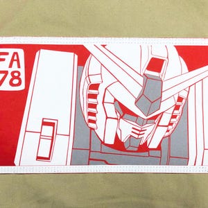May include: A rectangular patch featuring a robot's face in white and gray on a red background. The text "FA 78" is in white on the left side. The patch is on a khaki green fabric.