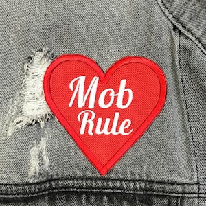 May include: A red heart-shaped patch with the words "Mob Rule" in white lettering on a gray denim jacket.