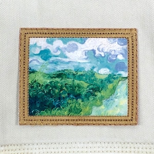 May include: A brown framed patch with a painting of a landscape with green hills, trees, and a blue sky with white clouds.