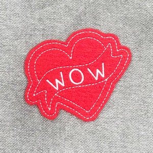 May include: Red felt heart-shaped patch with white stitching and the word "WOW" in white lettering inside a banner.