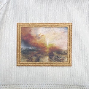 May include: A framed print of a painting depicting a stormy seascape with a bright light in the distance. The painting is in a gold frame with a textured surface.