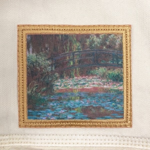 May include: A rectangular patch featuring a famous painting of a bridge over a pond with lily pads. The patch has a gold border and is set against a cream-colored fabric.