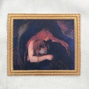 May include: A framed embroidered patch featuring a painting of a woman with long red hair, holding a small object in her arms. The painting is set against a dark background.