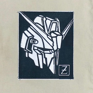 May include: A black and white graphic patch featuring a robot head design. The patch is rectangular with a black background and a white robot head. The letter "Z" is in a white square in the lower right corner. The patch is sewn onto a tan fabric.